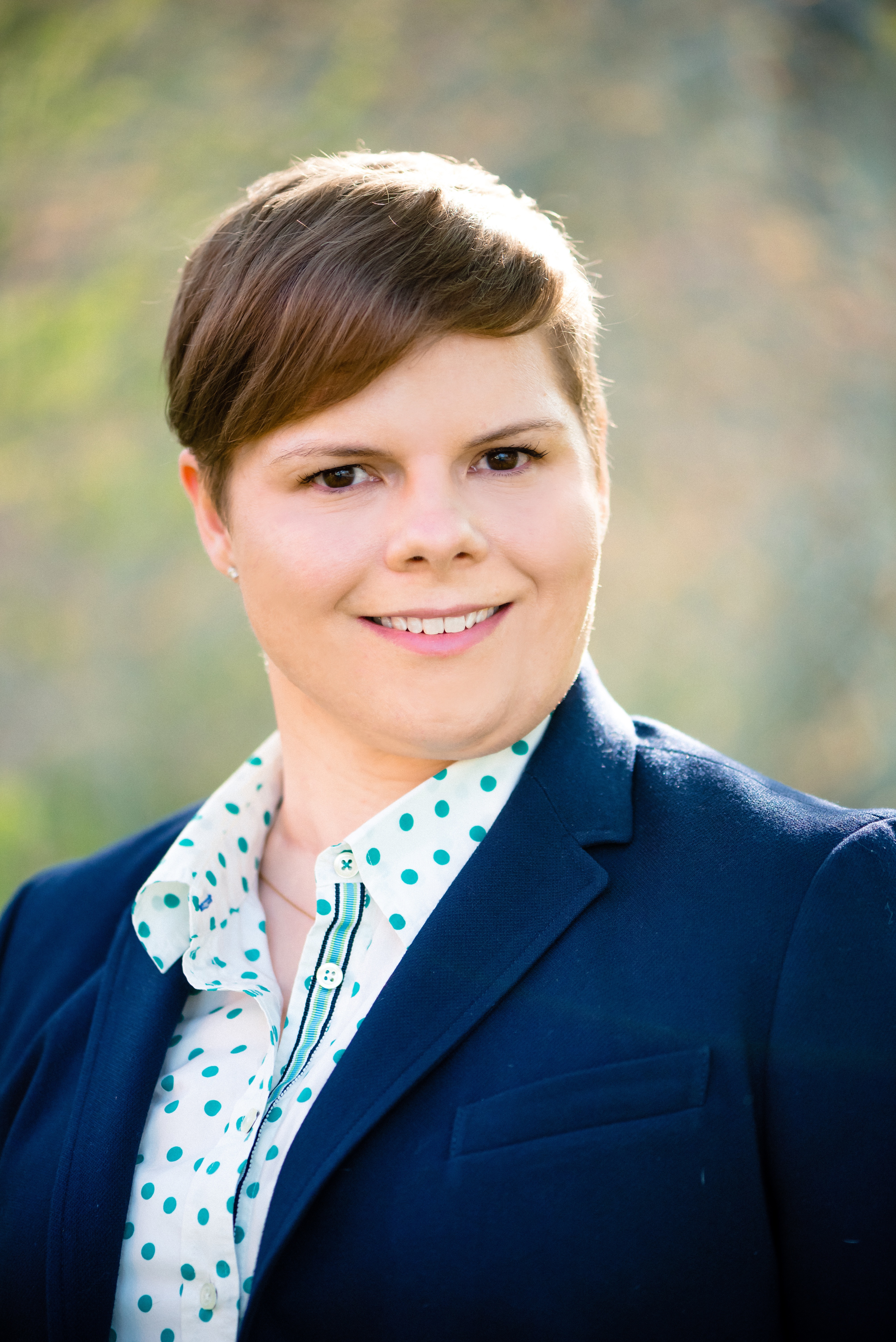 A headshot of Dr. Shaheen, a masculine-presenting white woman wearing a navy blue blazer.